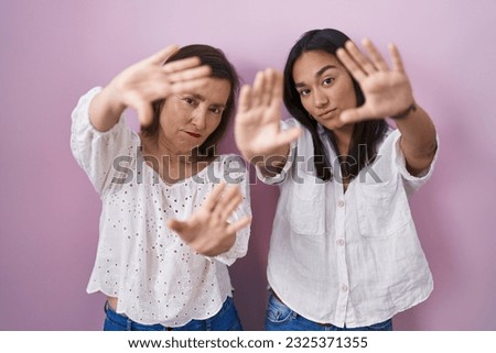 Hispanic mother and daughter together doing frame using hands palms and fingers, camera perspective 