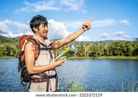 Young asian attractive male tourists looking for map in forest, Lost hiker male with backpacks reading travel map, Navigating and looking for directions in pine forest. Trekking concept.