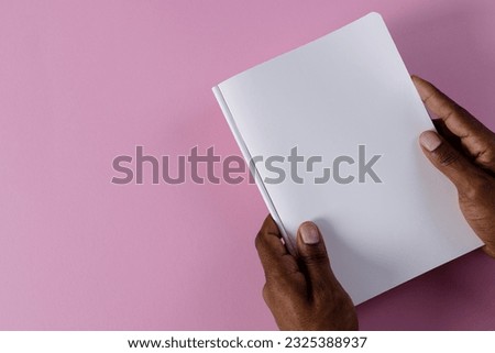 Hands of biracial man holding book with copy space on pink background. Literature, reading, leisure time and books.