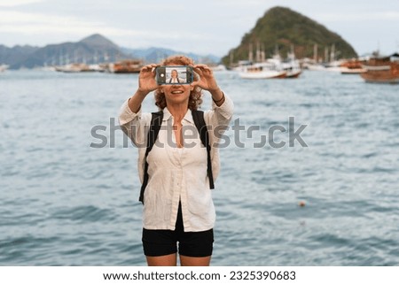 A young girl traveler makes a selfie on a mobile phone against the backdrop of a sea bay with yachts and islands.