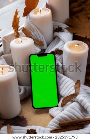 Green screen chromakey mobile phone app copy space on background of aesthetic atmosphere Autumn leaves spices and candle on knitted white sweater in warm yellow lights. Still life. Raining