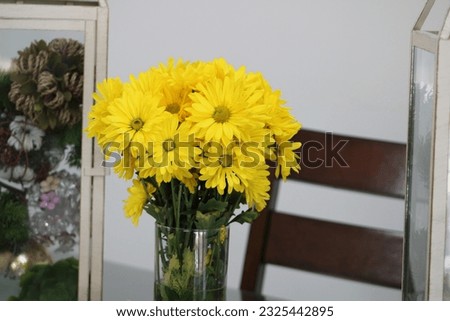 A bouquet of yellow mums that are in a vase on a dining room table.