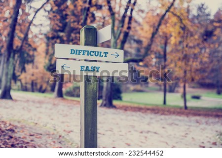 Signpost in a park or forested area with arrows pointing two opposite directions towards difficult and easy, concept of different levels of difficulty. Royalty-Free Stock Photo #232544452