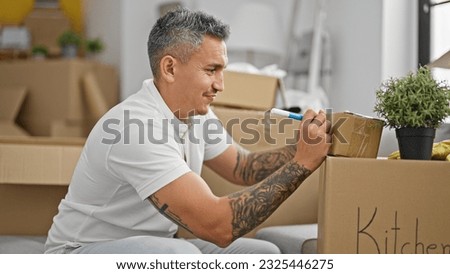 Young hispanic man sitting on sofa writing on package at new home