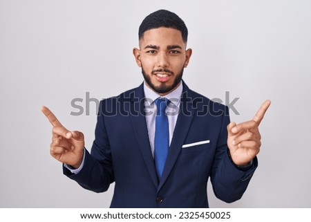 Young hispanic man wearing business suit and tie smiling confident pointing with fingers to different directions. copy space for advertisement 