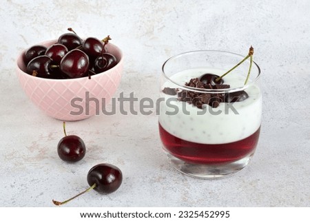 chia pudding with cherry jelly and chocolate in drinking glass and bowl of cherries 