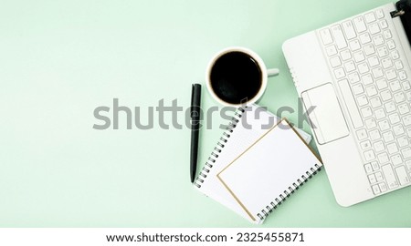 Opened computer on the table, white cup of coffee, notepad and pen, office supplies.  Flat lay on green background, office work concept, back to school, webinars, online learning. Top view.