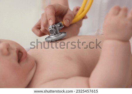 Pediatrician examining little baby with stethoscope in clinic, closeup