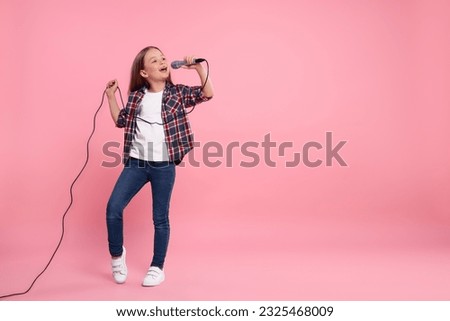 Cute little girl with microphone singing on pink background, space for text Royalty-Free Stock Photo #2325468009