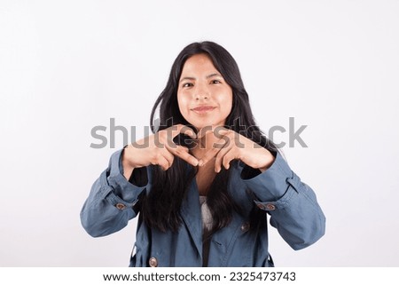 Photograph of young woman making a heart with her fingers on a light studio background. Concept of people and emotions