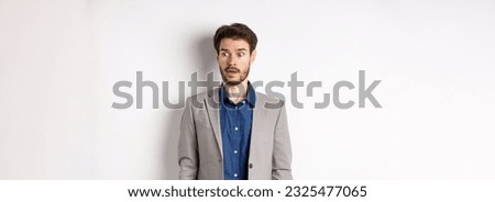 Shocked male entrepreneur in suit looking aside at logo with startled face, standing on white background. Royalty-Free Stock Photo #2325477065