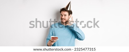 Celebration and holidays concept. Cheerful smiling man in party hat, celebrating birthday with bday cake, showing call me phone gesture near ear, white background.
