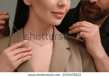 Man putting elegant necklace on beautiful woman against dark grey background, closeup Royalty-Free Stock Photo #2325478223