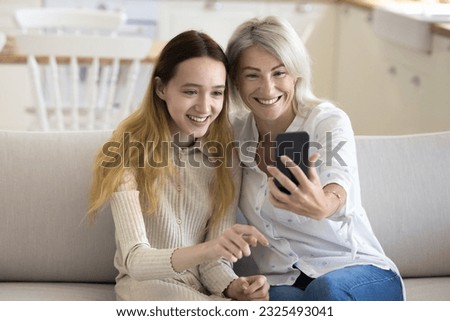 Happy teen grandkid and pretty blonde grandmother taking self picture on smartphone, having fun, smiling, laughing, posing for selfie on mobile phone, enjoying family leisure, friendship