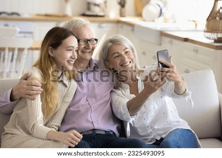 Happy grandma and grandpa hugging teenage child, holding mobile phone, taking family selfie photo, video together, smiling, laughing, using Internet media technology