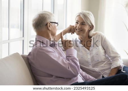 Positive senior wife listening to speaking husband. Older retired couple sitting on couch at home, talking, enjoying conversation, leisure, discussing retirement, smiling, laughing Royalty-Free Stock Photo #2325493125