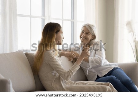 Happy mature grandma talking to teenage grandkid girl, sitting on couch, listening to speaking kid, smiling, laughing, enjoying conversation, trust, friendship, family relationship Royalty-Free Stock Photo #2325493195