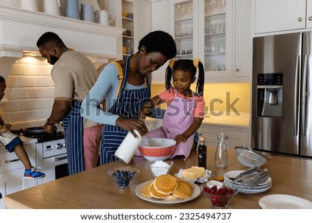 African american mother and daughter mixing batter in bowl while father and son making pancakes. Unaltered, lifestyle, family, love, togetherness, childhood, food, preparation and kitchen concept.