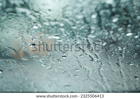 A small raindrop rests on the glass of car after rain. Rain drops on window glasses surface with cloudy background. Natural Pattern of raindrops. Copy space for text.