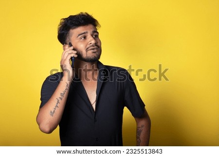 Guy talking on a phone with a little smile on his face, Stylish Male Model Standing Against Vibrant Yellow Background, Holding Phone in Hand,
