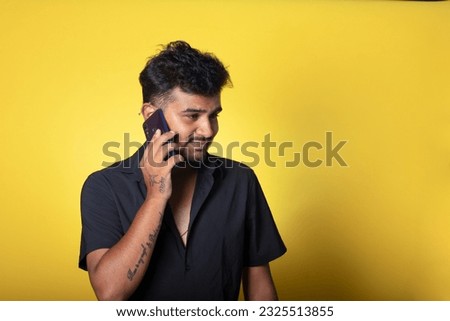 Guy talking on a phone with a little smile on his face, Stylish Male Model Standing Against Vibrant Yellow Background, Holding Phone in Hand,