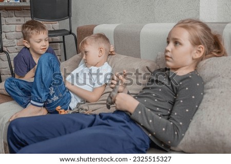 two little boys and a little girl are watching TV together, sitting on the sofa in the living room. Children's leisure, videos and cartoons for primary school children.