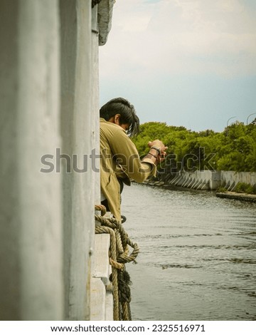 young asian man aiming his camera out the window of the ship at the port of Sunda Kelapa. Jakarta, Indonesia : November 13, 2022.