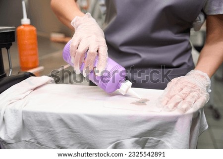Woman in protective gloves applying solvent into spot on t-shirt Royalty-Free Stock Photo #2325542891