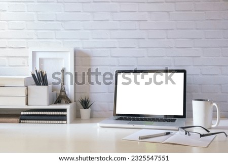 Simple workplace with laptop, cup of coffee, picture frame and houseplant on white table.