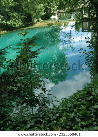A green-blue lake surrounded by greenery, the sun shines on it, the trees reflect in the water