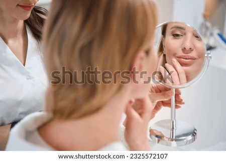 Client of a cosmetology clinic examines her face in mirror Royalty-Free Stock Photo #2325572107