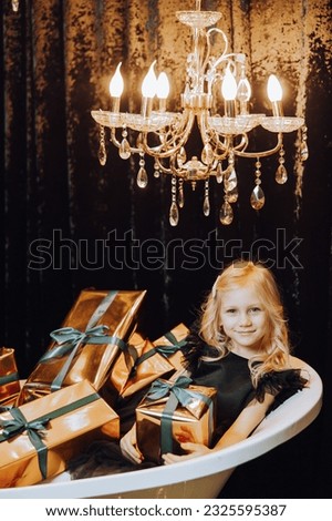 Merry Christmas and Happy Holidays! Cheerful little girl in a bath with Christmas presents in gold wrappers. Children are having fun. Loving family with gifts in the room.