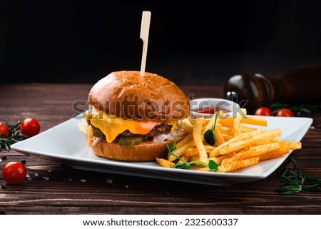 Cheeseburger with beef, tomato, pickles cucumber, red onion, lettuce, cheddar cheese, ketchup and French fries. Tasty burger cooking with beef, tomato, cheese, cucumber and lettuce. Royalty-Free Stock Photo #2325600337