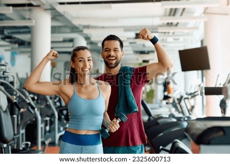 Happy athletic couple flexing their muscles after working out in a gym and looking at camera. Royalty-Free Stock Photo #2325600713