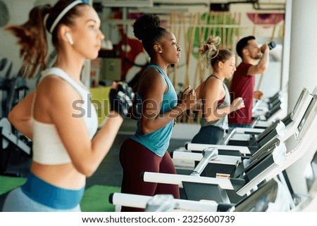 Group of young athletes running on treadmill during sports training in a gym. Focus in on African American woman. Royalty-Free Stock Photo #2325600739