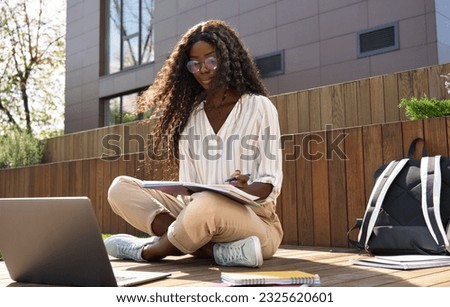 Black young woman model, pretty curly African female university student elearning using laptop computer studying outdoors in park on sunny day, remote learning digital online education, candid shot.