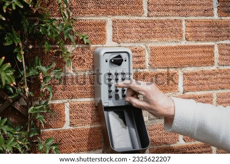 Buttons being pressed by a senior woman on a heavy duty, wall mounted key safe on an exterior brick wall.  Royalty-Free Stock Photo #2325622207