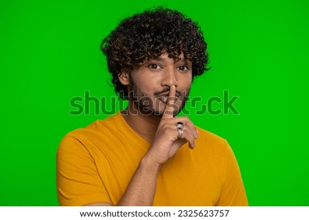 Shh be quiet please. Young indian man presses index finger to lips makes silence gesture sign do not tells secret, stop gossip. Handsome bearded hindu guy isolated alone on chroma key background