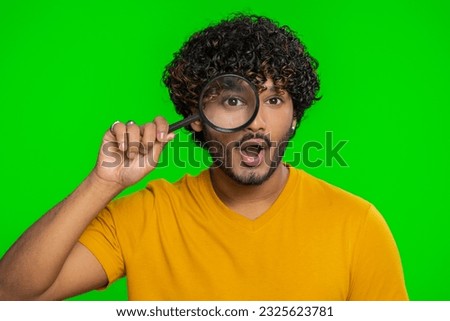 Investigator researcher scientist man holding magnifying glass near face, looking into camera with big zoomed funny eyes, searching, analysing. Handsome indian guy isolated on chroma key background
