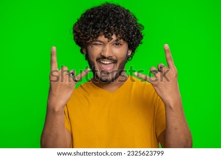 Overjoyed young indian man showing rock n roll gesture by hands, cool sign, shouting yeah with crazy expression, dancing, emotionally rejoicing in success. Hindu guy isolated on chroma key background