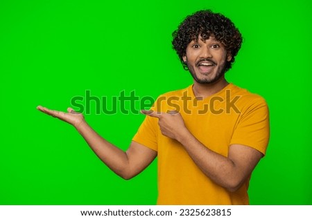 Happy young indian man showing thumbs up and pointing empty place, advertising area for commercial text inscription, copy-space for goods promotion banner. Hindu guy isolated on chroma key background