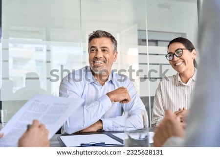 Happy diverse business people international corporate executive team talking at group meeting. Smiling older Latin male manager working with colleagues collaborating at boardroom table. Royalty-Free Stock Photo #2325628131