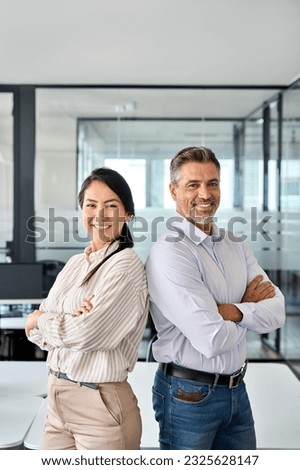 Happy confident professional mature Latin business man and Asian business woman corporate leaders managers standing in office, two diverse executives team posing arms crossed, vertical portrait. Royalty-Free Stock Photo #2325628147