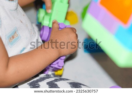 Child holds colorful toy, fingers engaged. Cheerful, happy. Indoor close-up. Alone. Fun.