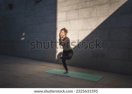 One adult caucasian woman doing yoga practice in summer day outdoor in the city in front of the wall with shadow and sun healthy lifestyle wellbeing concept self care