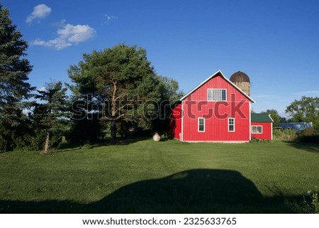 the shadow of a family SUV against the green grass during a roadtrip in the country with a bright red farm building in the background