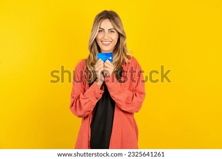 Photo of young beautiful blonde woman standing over yellow studio background positive smile hold credit card income salary