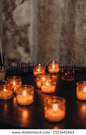 Picture of Easter candles burning at night with golden light of candle flame. Lampion candles glowing in a dark church. Emotional mood. Many burning candles with shallow depth of field
