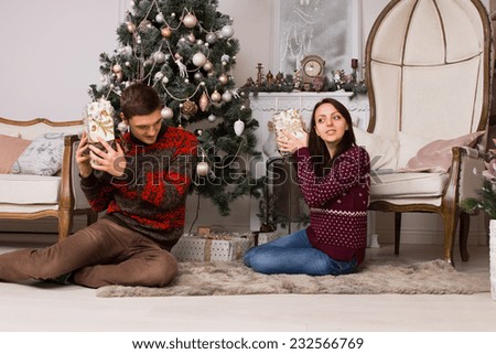 White Young Partners Sitting on the Floor While Listening Gift Box Contents Near the Christmas Tree and Large Royal Chair.