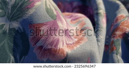 Wavy light blue fabric with pink, purple and green floral print of pink roses, in folds (macro, texture).
